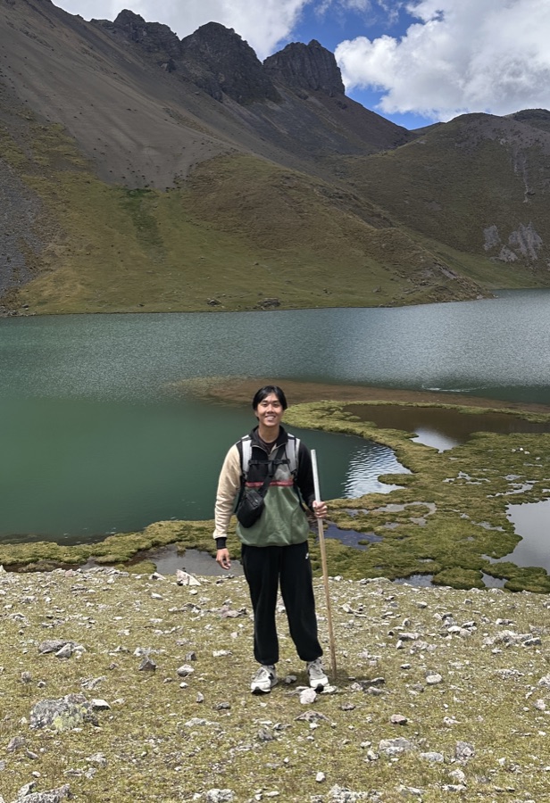 Eric standing by an alpine lake in the mountains, holding a hiking stick